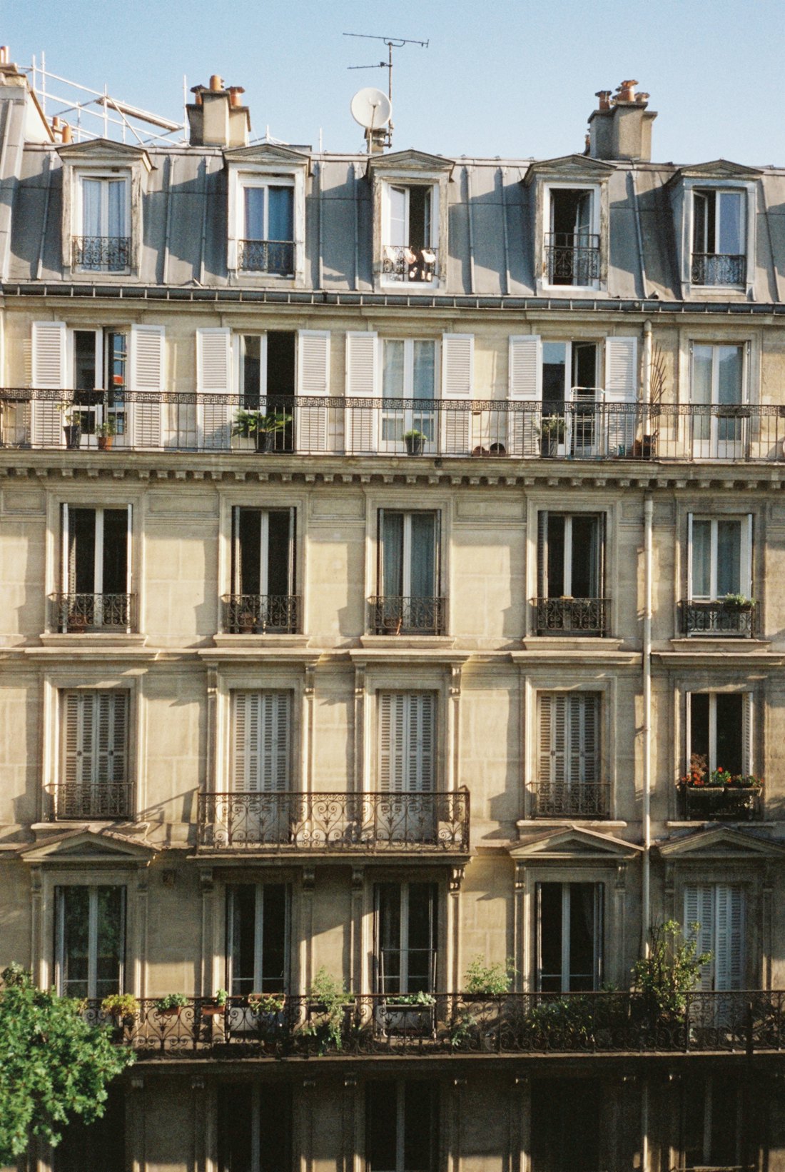 Façade d'un immeuble haussmannien au soleil, volets et balcons en fer forgé